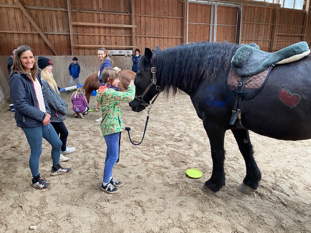 Mehrere Kinder in einem Reitstall mit einem schwarzen Pferd.